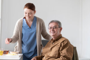 Caregiver assisting elderly man with meal in home setting, highlighting personal care and support for dementia patients in hospice.