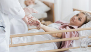 A compassionate healthcare provider holding the hand of a female patient in a hospital bed, offering comfort and support.